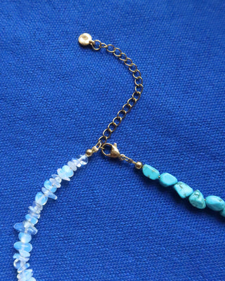 Necklace with turquoise howlite and white moonstone beads and a gold extender with lobster claw clasp on a blue background