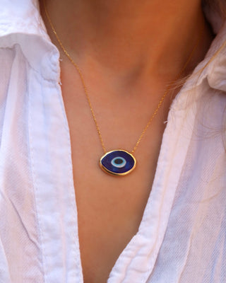 Woman wearing a gold-plated sterling silver necklace with a dark blue Murano glass evil eye pendant made in Greece, Greek jewelry