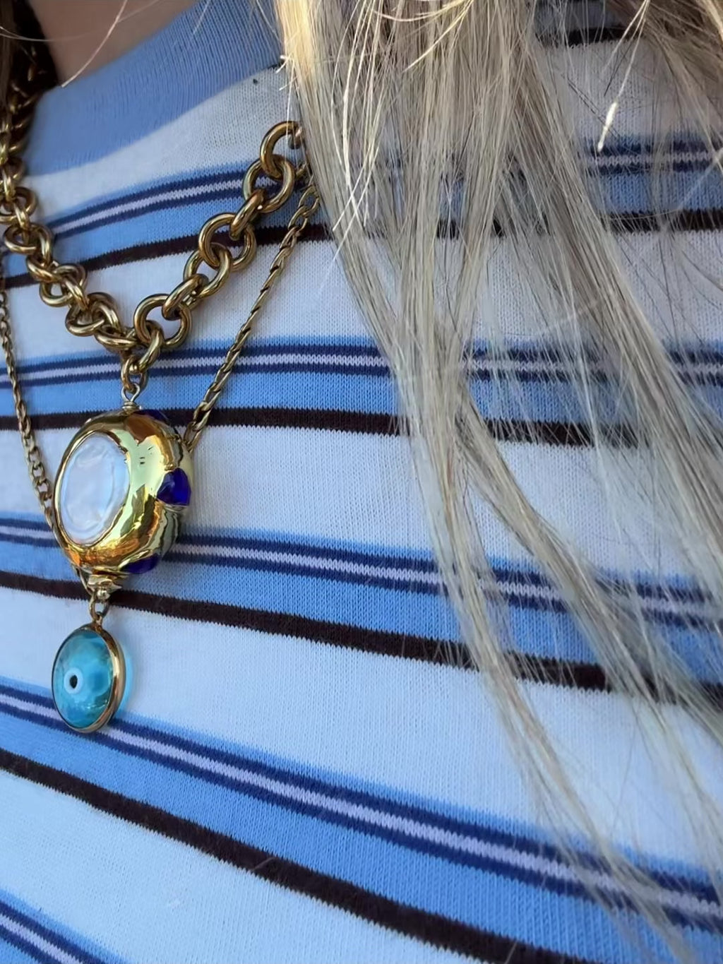 Woman wearing a gold chunky chain statement necklace with a jumbo freshwater pearl drop pendant with blue zircon stones surrounding it made in Greece. Greek jewelry