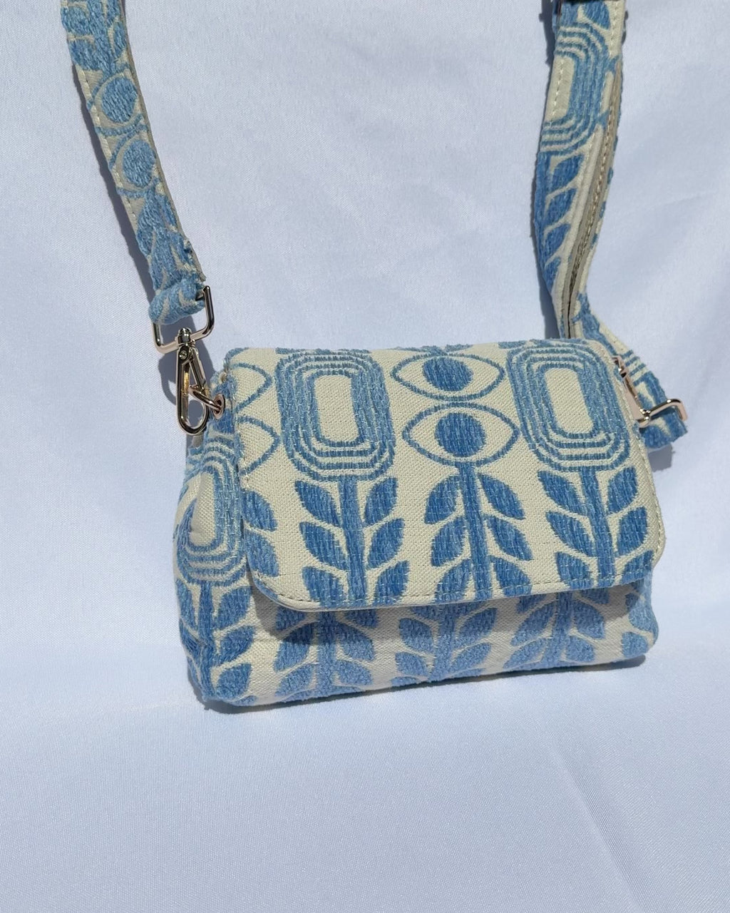 A blue and white patterned crossbody bag with gold hardware featuring evil eyes and olive branches handmade in Greece. Emily in Paris handbag