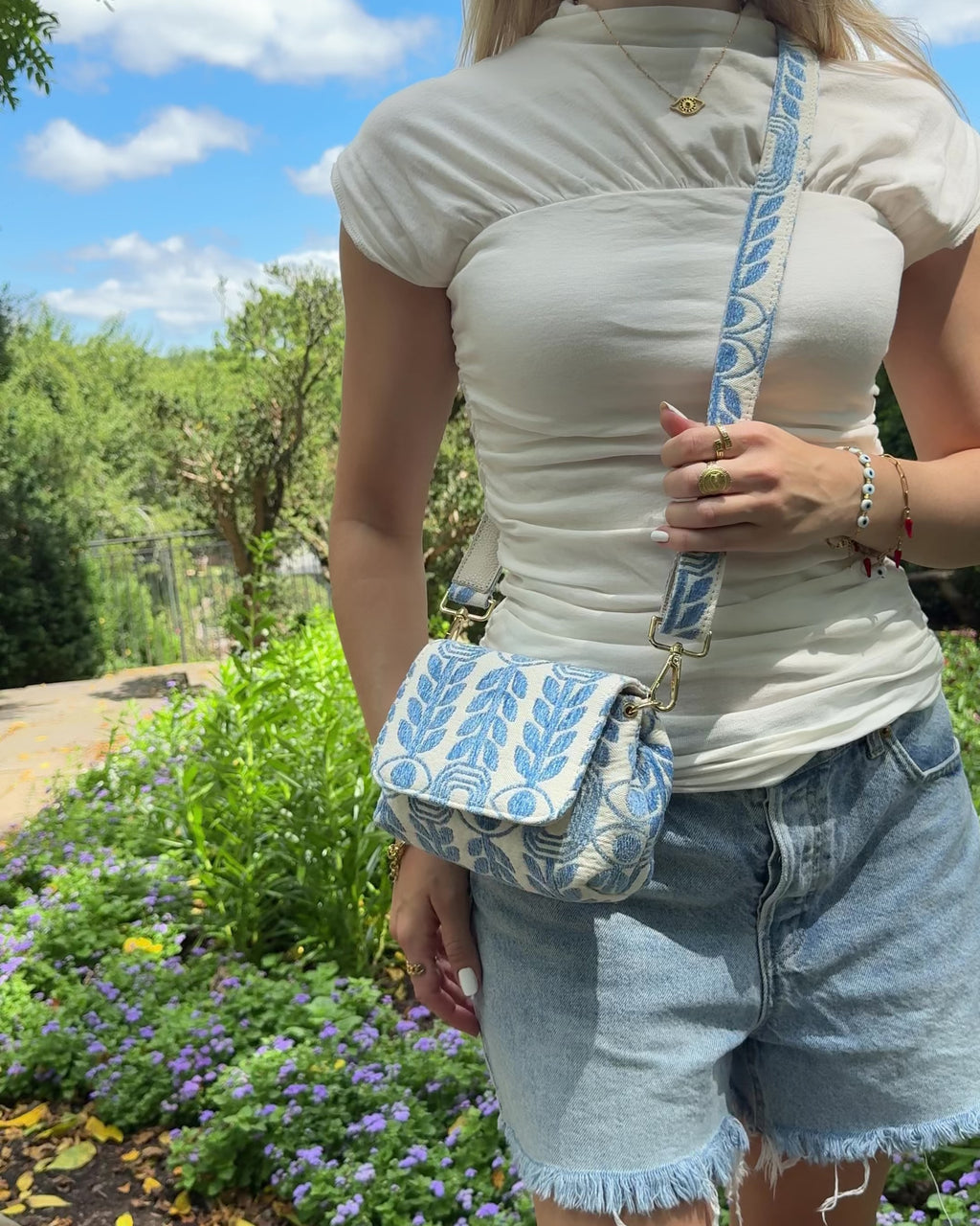 Woman wearing a light blue and cream printed with evil eye and olive branch designs with a cream top and denim shorts
