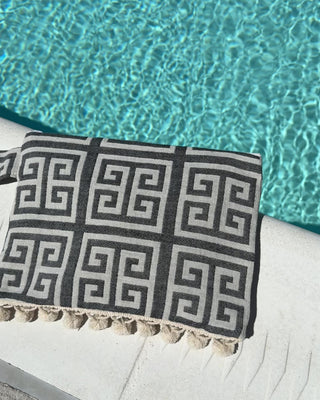 black and white greek key wet/dry zipper pouch clutch bag with cream pom pom trim next to a pool