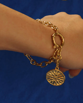 Gold chain bracelet with a Vergina sun coin charm on a blue background made in Greece, Ancient Greek jewelry