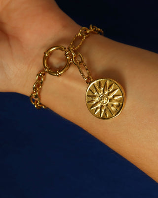 Gold chain bracelet with a Vergina sun coin charm on a blue background made in Greece, Ancient Greek jewelry