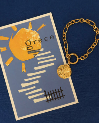 Gold bracelet with a round Vergina sun charm on a Greece postcard featuring a sun