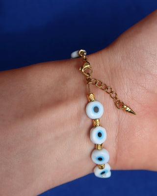 Bracelet with eye-shaped beads and gold chain on a wrist against a blue background, Greek evil eye bracelet