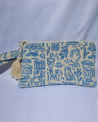 Wristlet clutch bag with a light blue Greece inspired print featuring the Parthenon, owls, vases, ancient Greek scultures, olive trees and more. Made in Greece with a tassel, zipper closure, and wrist strap