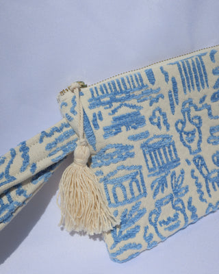 Wristlet clutch bag with a light blue Greece inspired print featuring the Parthenon, owls, vases, ancient Greek scultures, olive trees and more. Made in Greece with a tassel, zipper closure, and wrist strap
